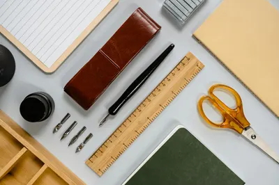 Flat lay of stylish desk stationery including pens, notebooks, and tools.