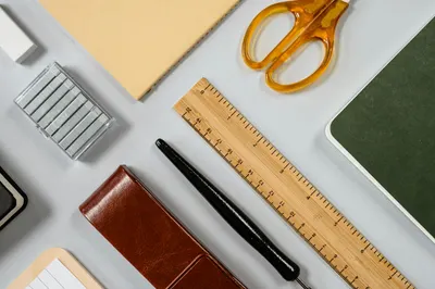 A neatly arranged flat lay of office supplies including scissors, ruler, fountain pen, and notebooks.