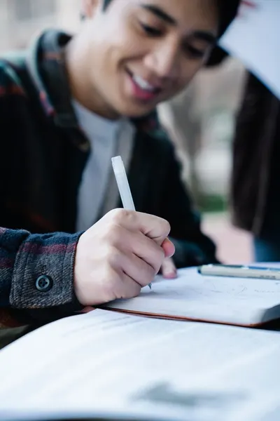 Close-up of a young adult writing in a notebook with a pen outdoors.