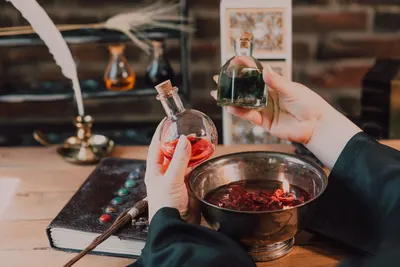 Hands mix colorful potions in a wizarding world themed setup with spellbook and wand.