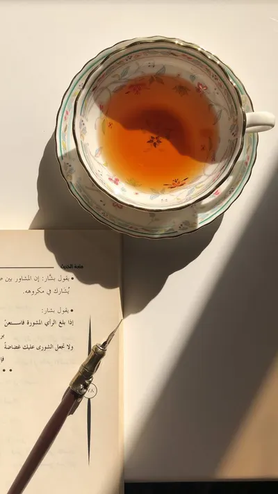 A cozy flatlay featuring a floral teacup filled with tea, alongside a calligraphy pen and book.