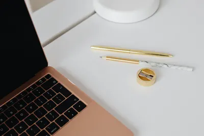 Elegant workspace featuring a gold pen, marble pencil, sharpener, and laptop on a white desk.