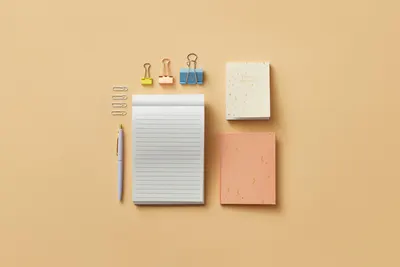 A minimalist flat lay of office supplies on a beige background, including notepads and clips.