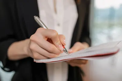 Businesswoman in black blazer taking notes with a pen on a notepad indoors.