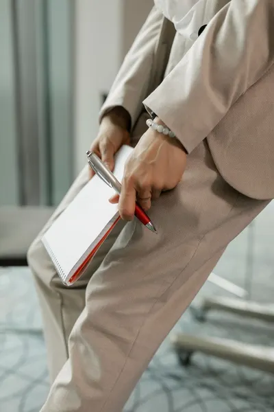Professional person in suit holding a notebook with a pen indoors, ideal for business contexts.