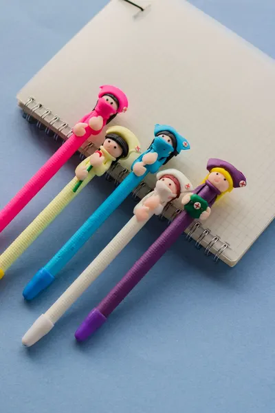 Top view of colorful pens with cartoon tops placed on a spiral notebook, offering a playful stationery vibe.