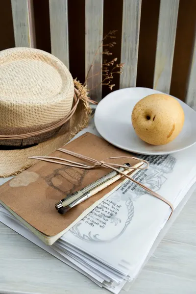 A stylish still life featuring a notebook with pens, a sun hat, and a pear.