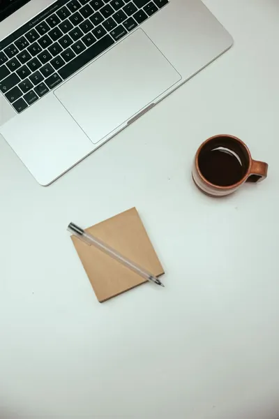 Top view of a minimalist desk setup with a laptop, coffee, and notepad.