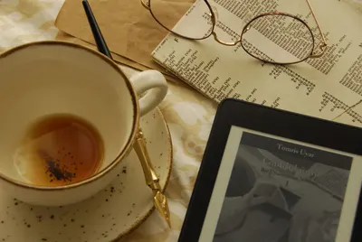 Cozy flat lay scene with tea, eyeglasses, and e-reader on a table.