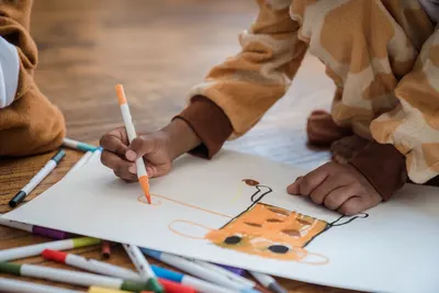 A child in pajamas draws with markers on paper indoors, showcasing creativity and play.