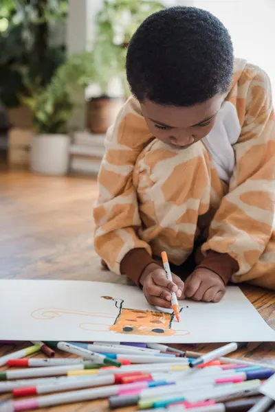 A young boy in animal pajamas creatively drawing with markers on paper indoors.