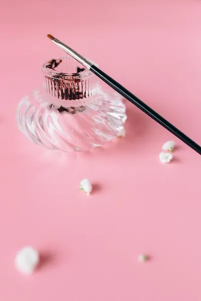 Stylish glass perfume bottle with a makeup brush on a pink backdrop, conveying elegance.