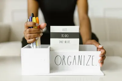 Close-up of hands organizing pens and notes in a white box labeled 'Organize.' Perfect for productivity inspiration.