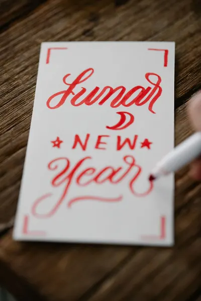 Close-up of a handwritten Lunar New Year card in red calligraphy on a wooden table.
