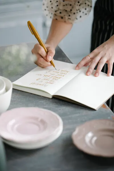 Close-up of hands writing in a notebook on a table with pink plates.