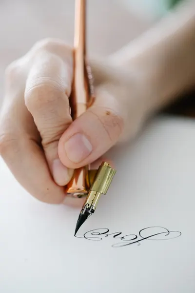 Close-up of a hand elegantly writing calligraphy with a dip pen on white paper.