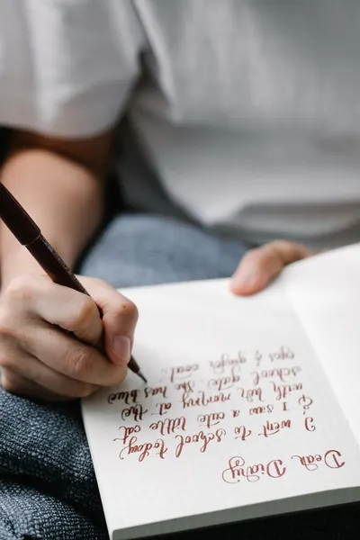 Close-up of a person writing calligraphy in a journal with a pen on a lined notebook.