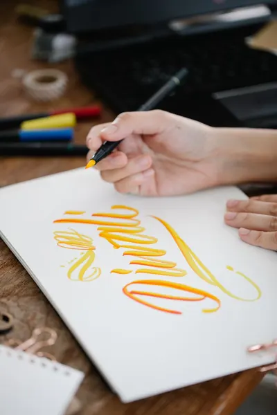 Close-up of hand crafting colorful calligraphy on paper with ink pens in an artistic setup.