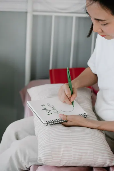 Person practicing calligraphy skills with green pen on notepad indoors.