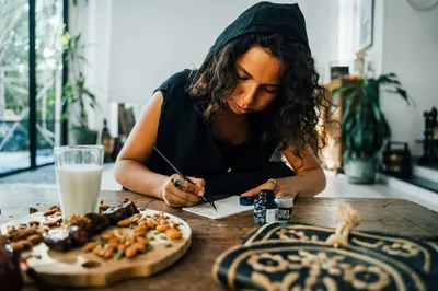 Young woman writing with calligraphy tools at a wooden table, displaying creativity and concentration.