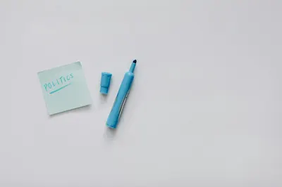 A flat lay of a blue marker and sticky note with 'politics' on a white surface.