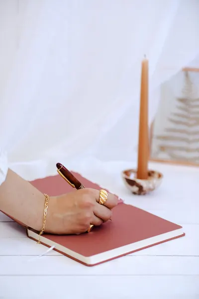 Close-up of a hand writing in a notebook with a pen in a minimalist setting. Warm and elegant.