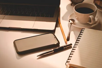 A warm workspace scene featuring a laptop, smartphone, coffee cup, and a notebook.