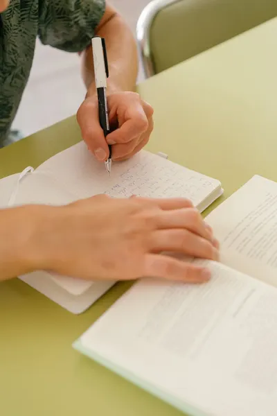 Close-up of a student diligently taking notes while reading a book.