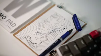 Close-up of a sketch on a clipboard with a blue pen on a tidy workspace.