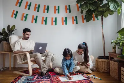 Family enjoying leisure time with drawing and laptop amidst Indian decor.