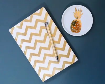 Stylish zigzag patterned notebook with a gold pen and decorative pineapple dish on blue surface.