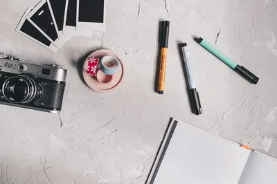Flat lay of a creative workspace featuring a camera, pens, washi tape, and Polaroids.