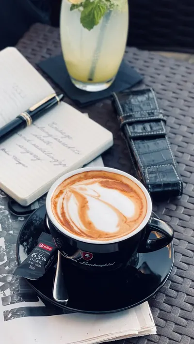 Latte art in a black cup on a table with a notepad and pen, creating a cozy setting.