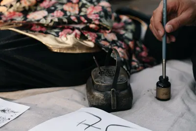 A hand using a calligraphy brush with ink beside traditional Asian art tools, conveying cultural heritage.