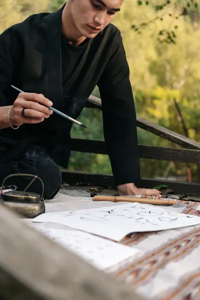 A man engaging in calligraphy with a brush on paper, set in a tranquil outdoor environment.